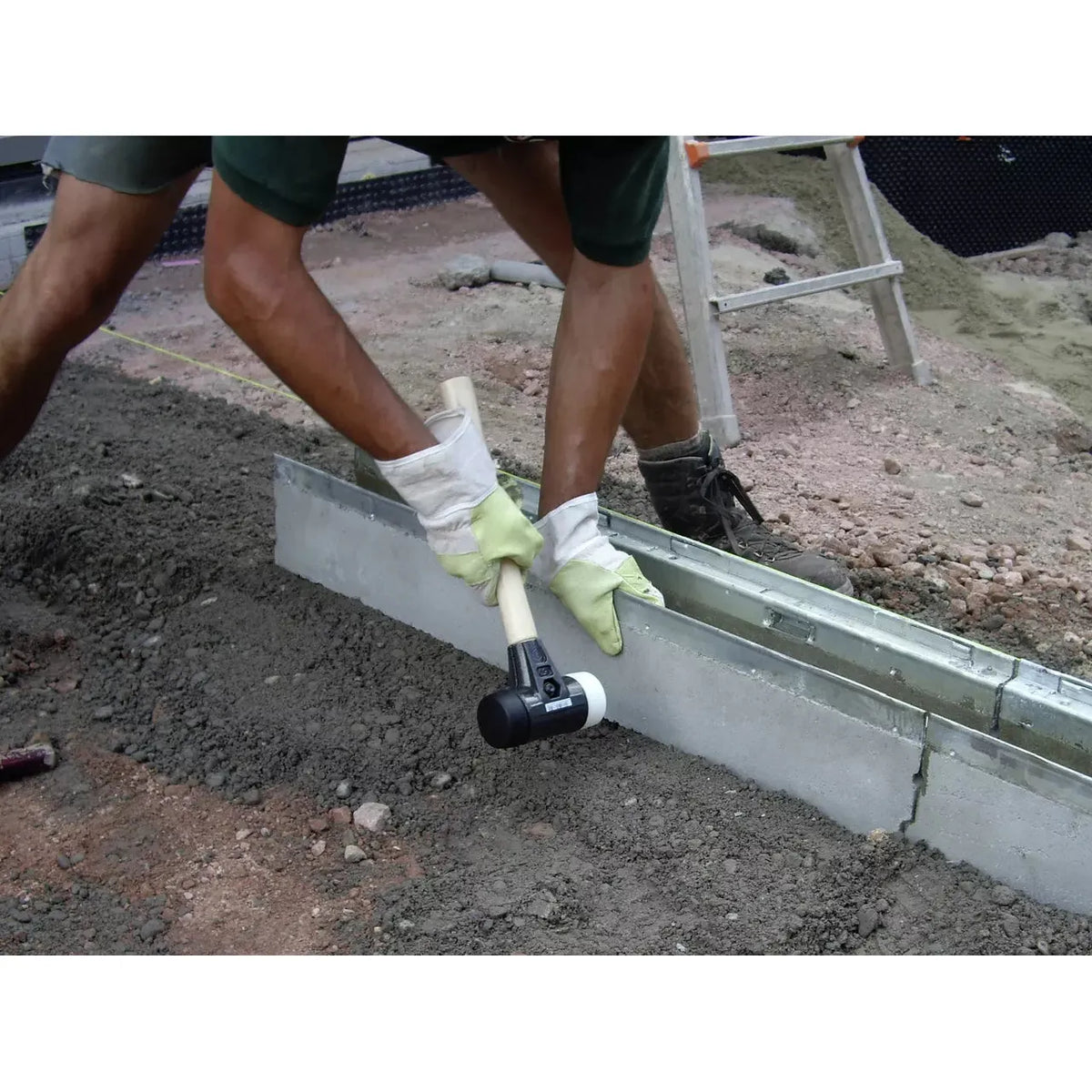 Person using a rubber mallet to adjust a concrete slab on a construction site.
