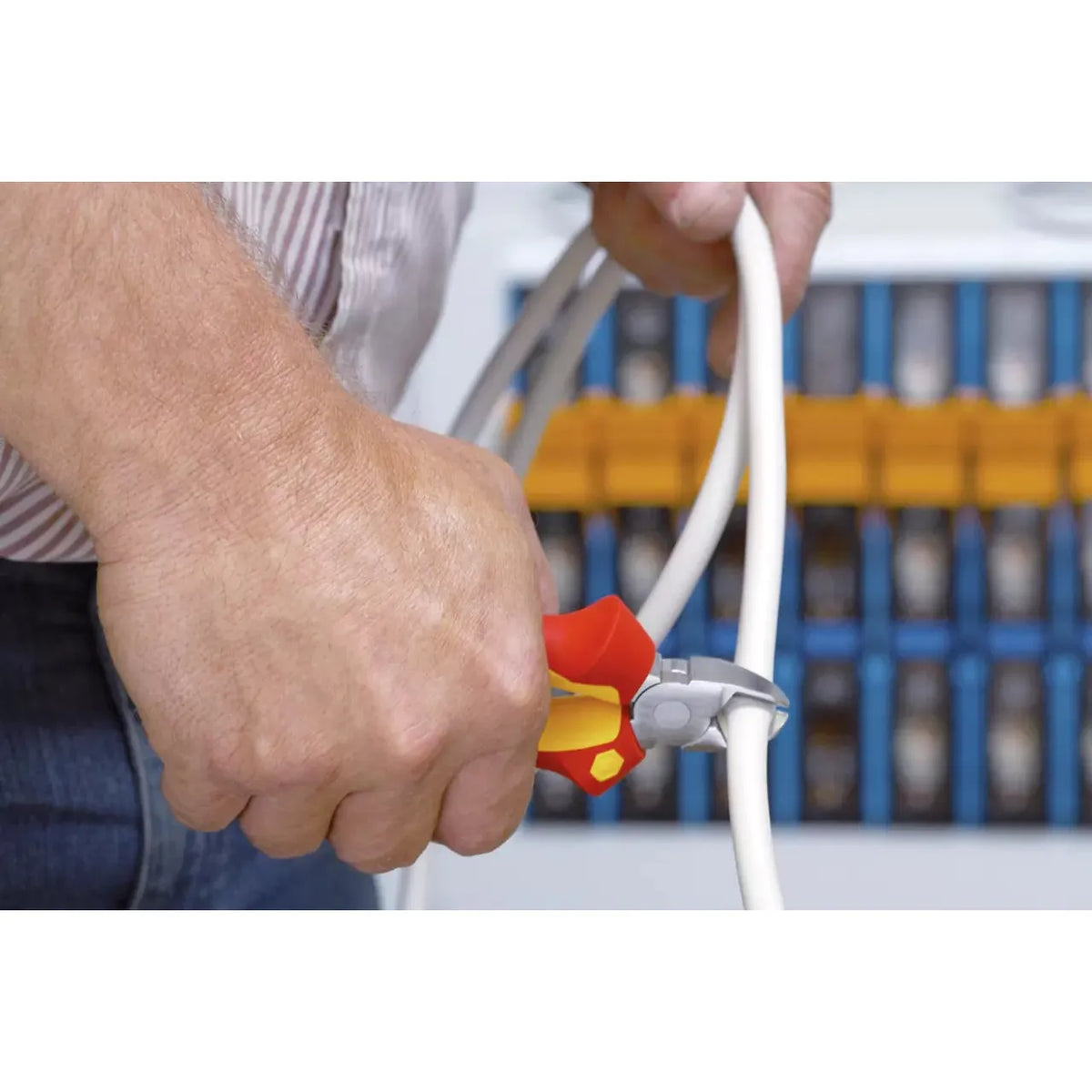 A person using red-handled side cutters to cut a white cable.