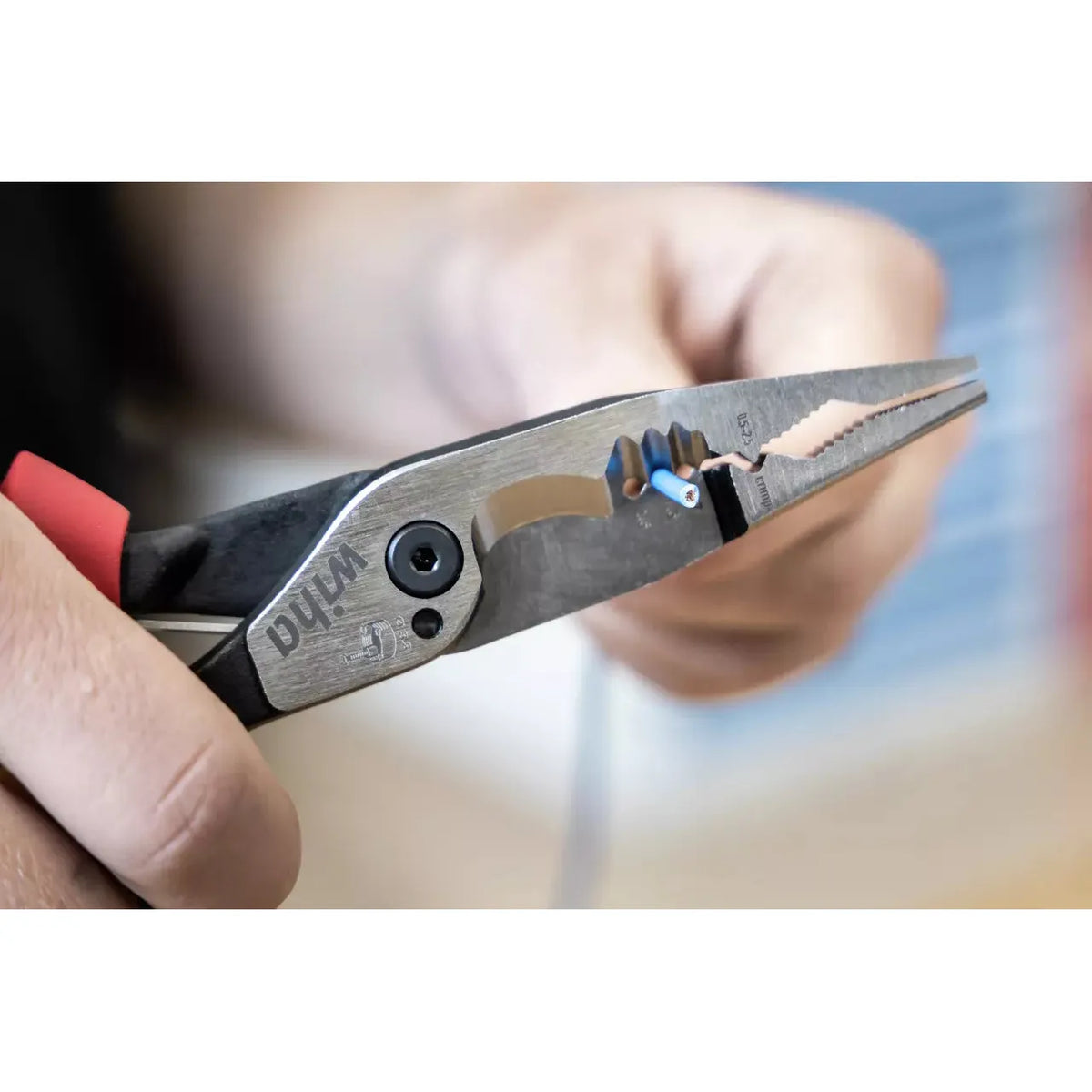 Person holding pliers with red handle, cutting blue wire