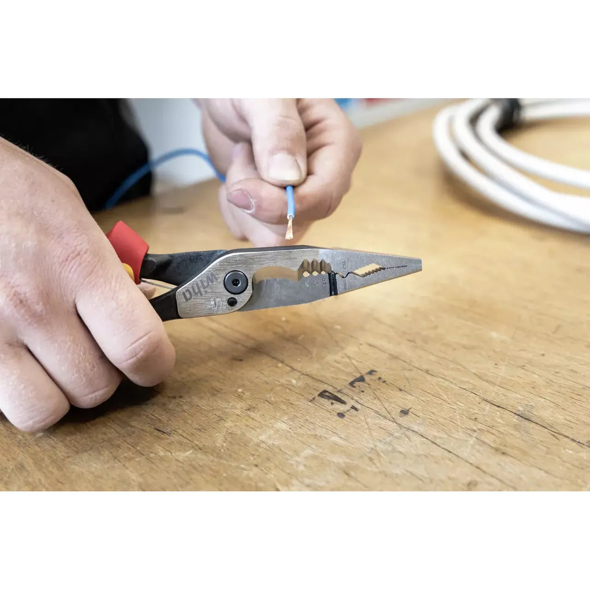 Person holding wire stripper and a cable on a wooden surface