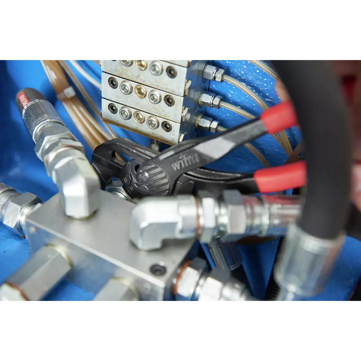 Adjustable pliers gripping a metal fitting amidst hydraulic connections.