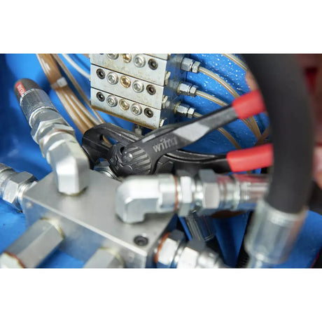 Adjustable pliers gripping a metal fitting amidst hydraulic connections.