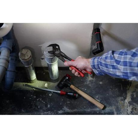 Person using adjustable pliers on a pipe, with tools on the floor.