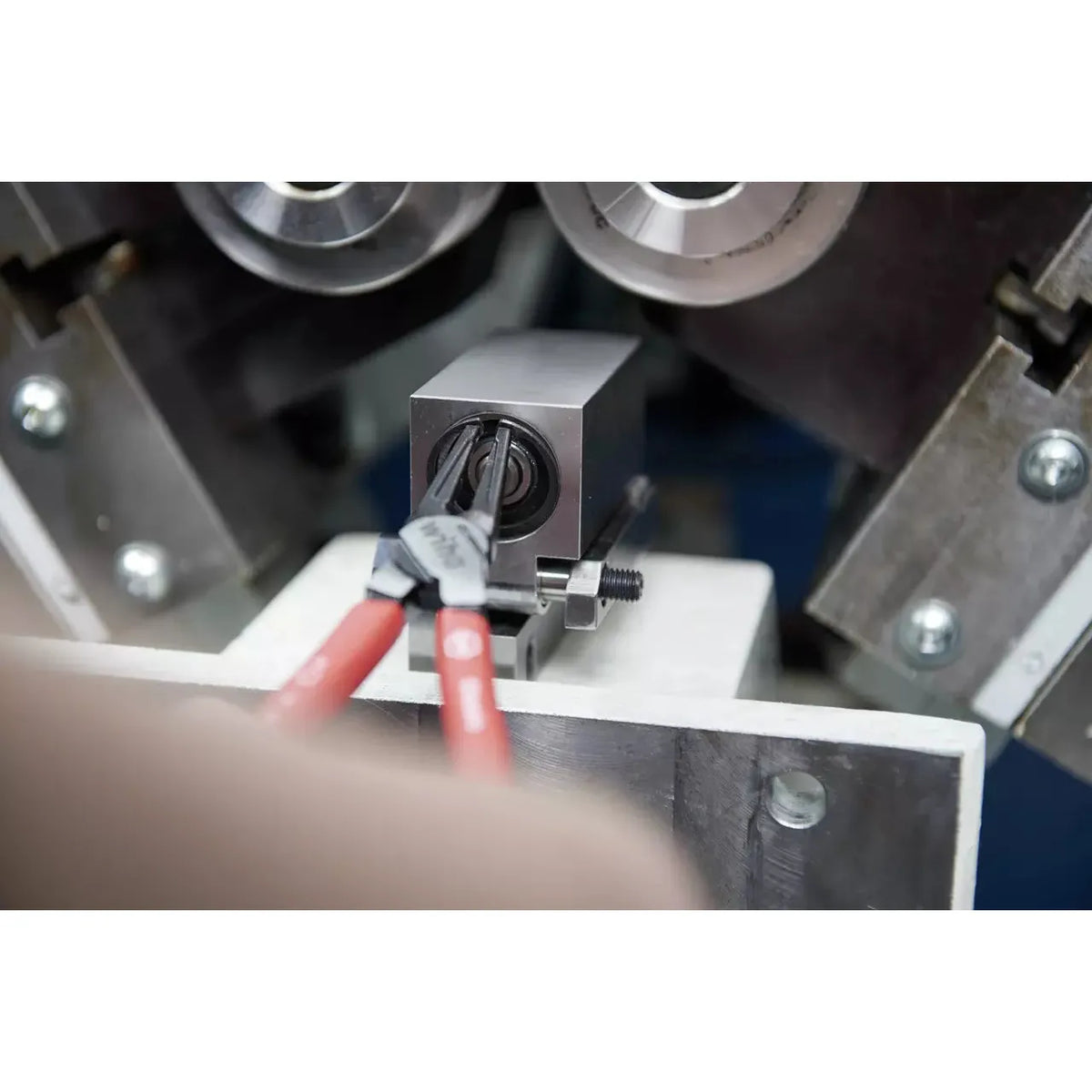 Pliers gripping a retaining ring inside a metal component with machinery in the background.