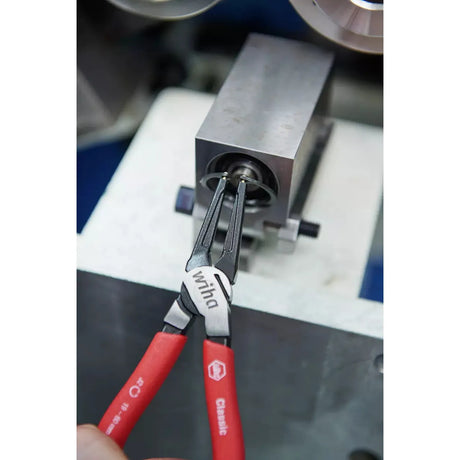 Red retaining ring pliers holding a metal retaining ring on a machine.