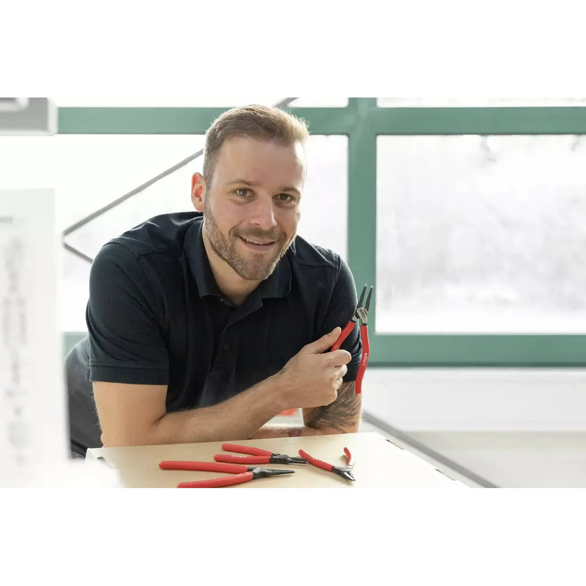 A person holding red-handled pliers, with more pliers on the table