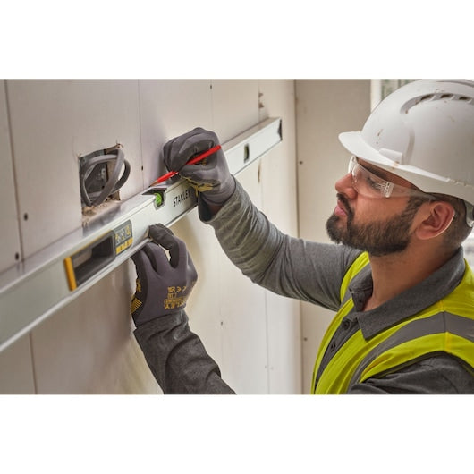 Stanley FMHT43678-1 spirit level used on drywall by a worker in gloves and safety gear.