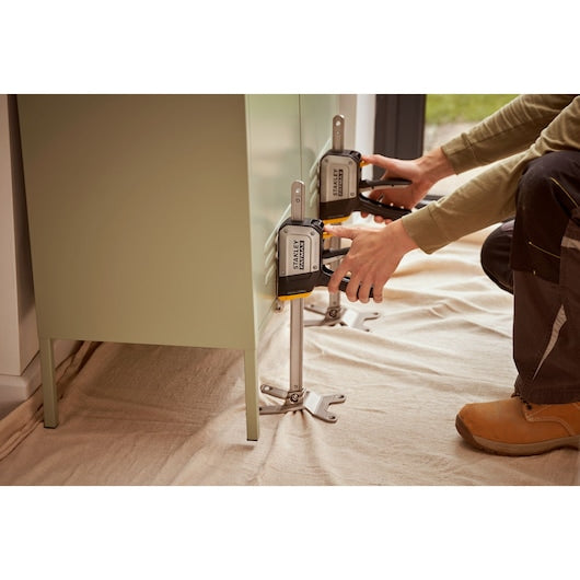 Photo of STANLEY FMHT83550-1 cabinet support clamp in use, holding a cabinet in place on a light fabric sheet.