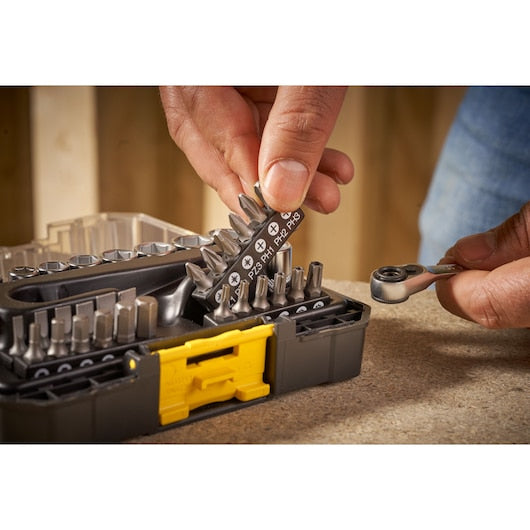 STANLEY FMMT19101-0 bit set with ratchet driver, close-up of hand selecting bit from black and yellow case.
