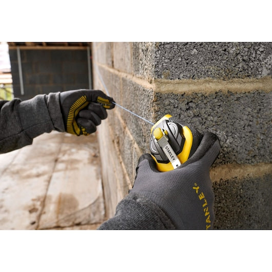 STANLEY STHT47311-0 chalk line reel in use on a brick wall, close-up of gloved hands pulling the blue line.