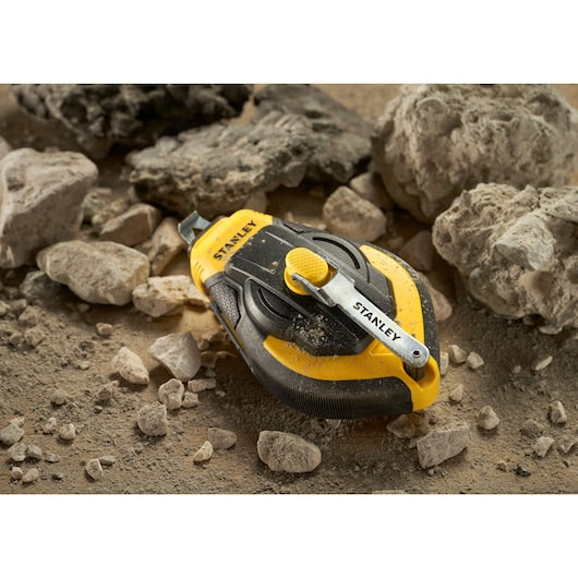 STANLEY STHT47311-0 chalk line reel, black and yellow, shown on dusty rocks.