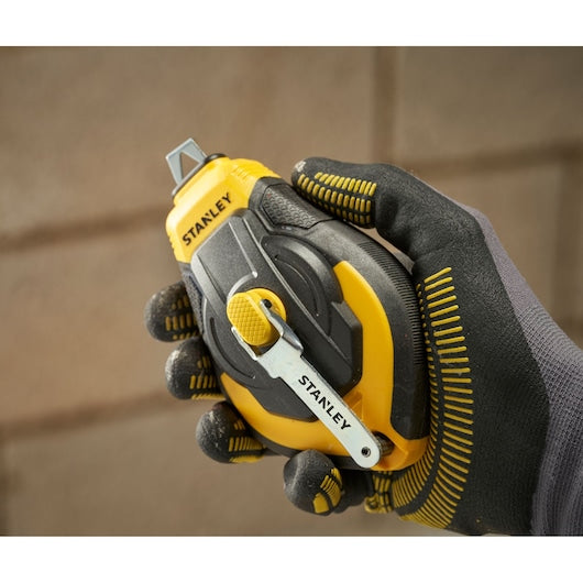 Stanley STHT47311-0 chalk line reel, yellow and black, held in a gloved hand, close-up view.
