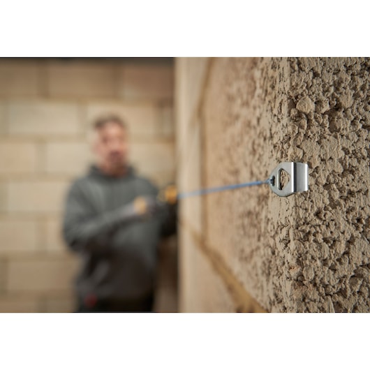 STANLEY STHT47311-0 chalk line holder attached to rough wall, blue chalk line stretched across surface.