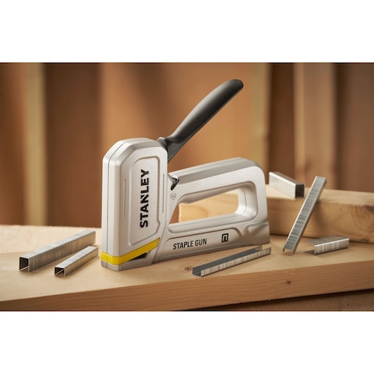 Stanley STHT70150-0 staple gun with black handle and metal staples on wooden surface, front angle.
