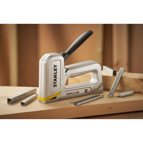 Stanley STHT70150-0 staple gun with black handle and metal staples on wooden surface, front angle.