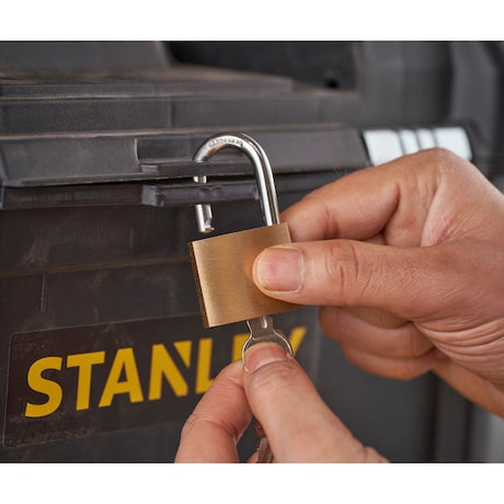 STANLEY STST1-80151 brass padlock being unlocked with a key on a black storage box, close-up.